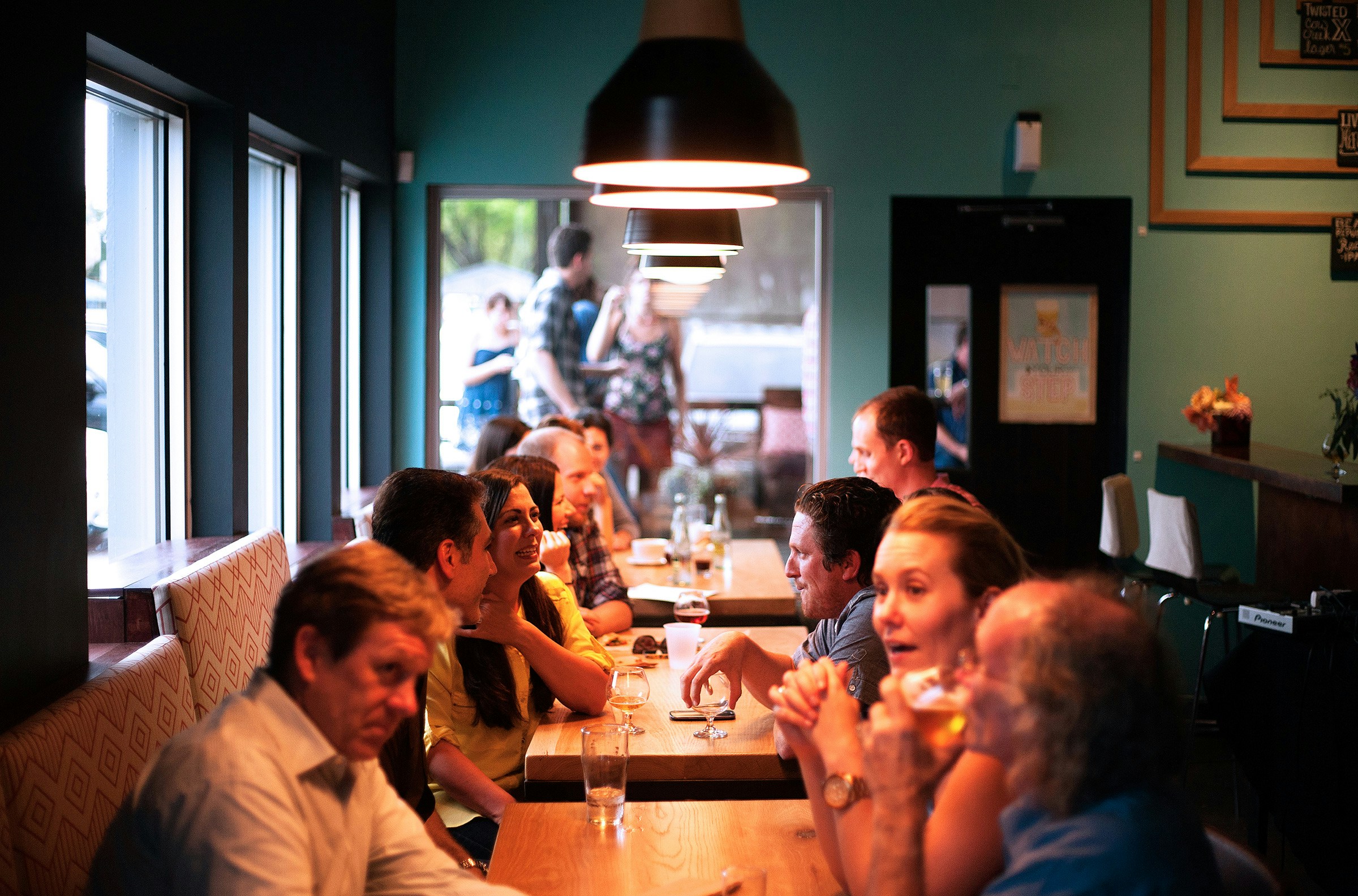 Group of people dining and socializing in a cozy, modern restaurant setting, with warm lighting and casual ambiance.