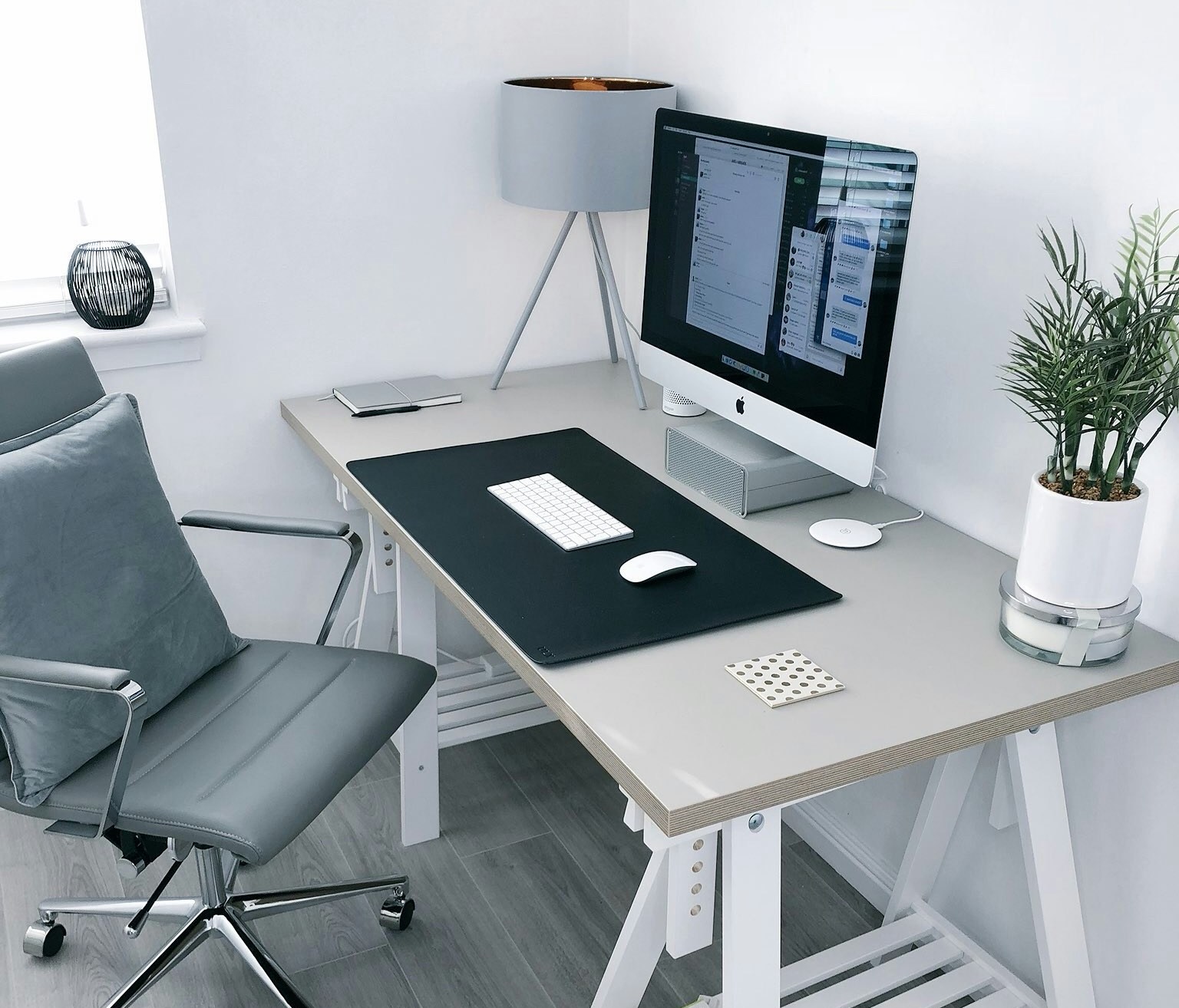 Modern home office setup featuring a sleek desk with a computer, minimalist décor, ergonomic office chair, desk lamp, and small plant in a bright, clean space.